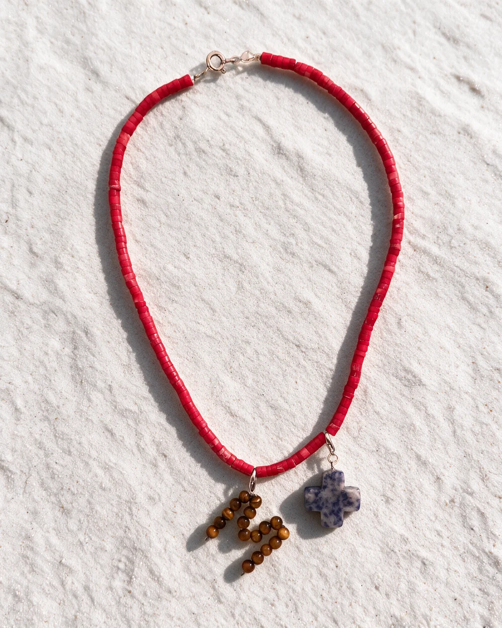 Spell necklace: a thin strand of red beads with a letter M made of tiger eye beads and a blue cross charm