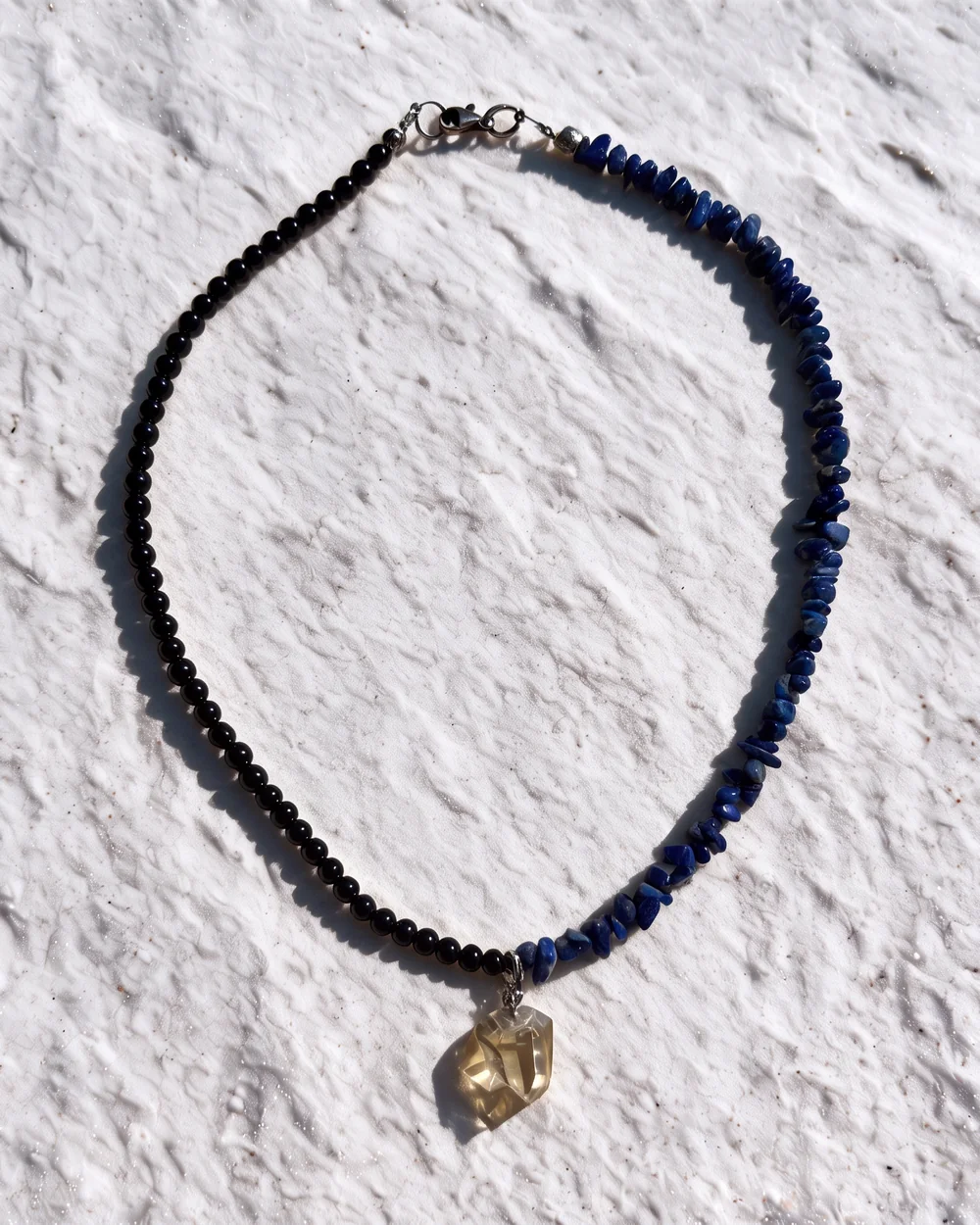 Split necklace: black beads on one side, blue stone chips on the other, with a clear yellow crystal pendant