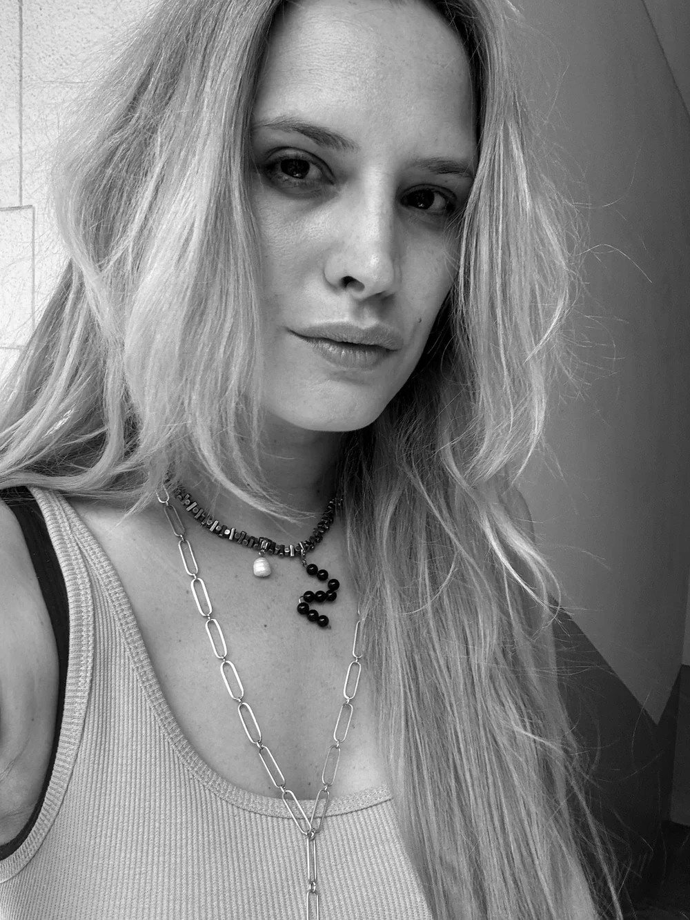 Black and white portrait of Zsófi wearing layered necklaces, one with a beaded black letter